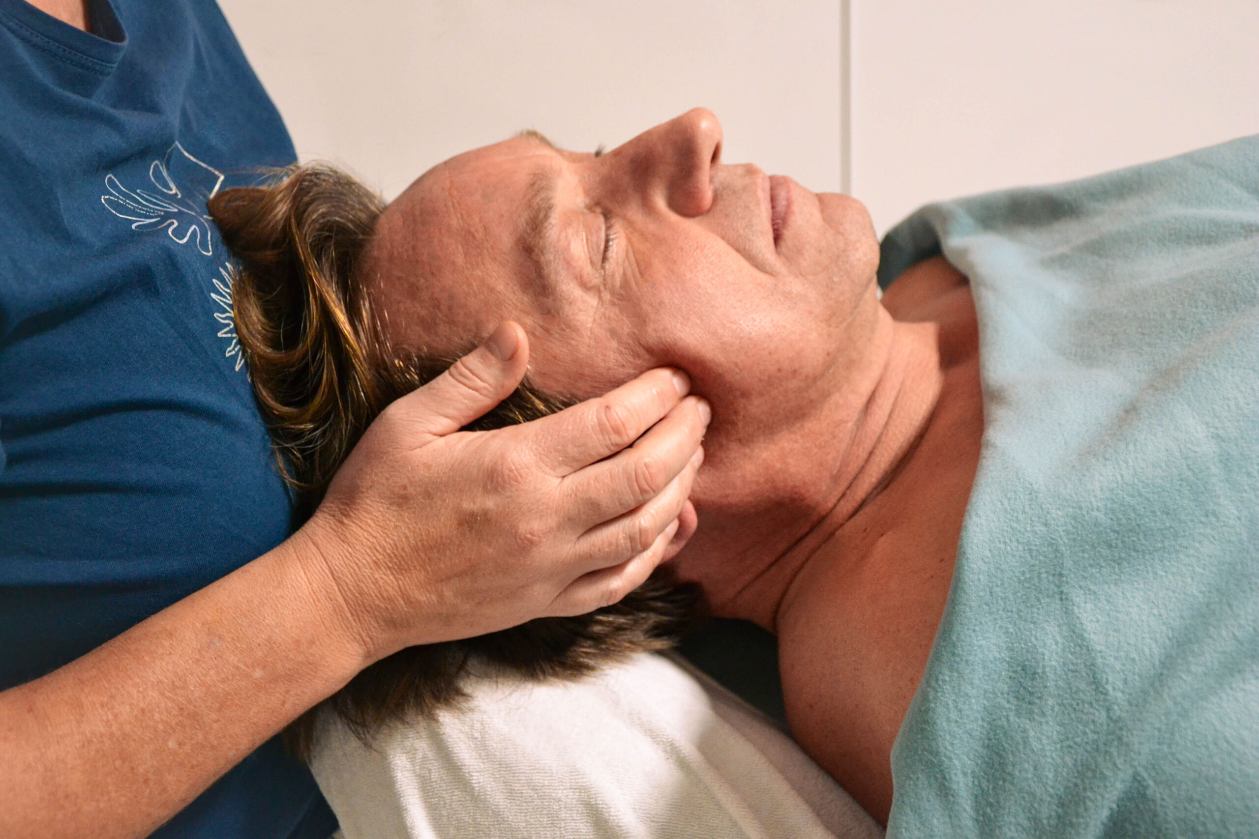 Das Bild zeigt den Kopf einer Person in den Händen der Therapeutin, die den Kiefer von außen mit Druck behandelt